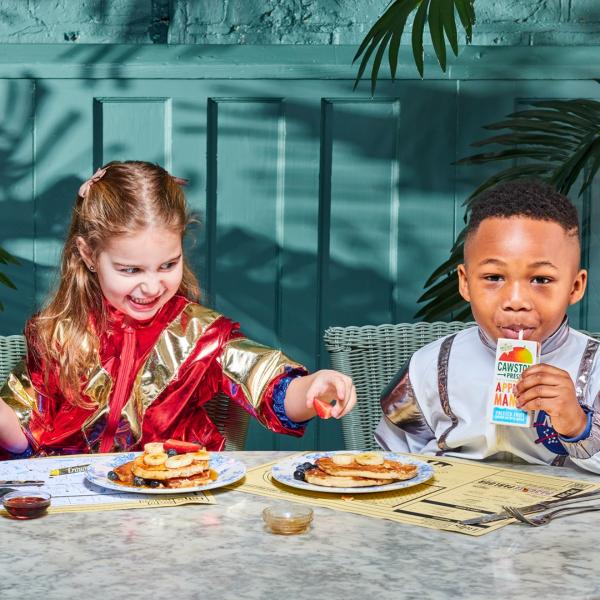 Two children in superhero costumes eating pancakes